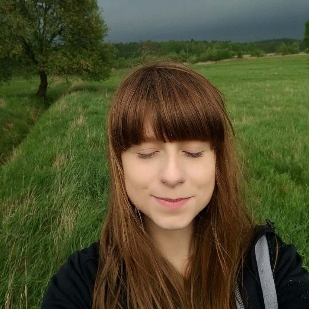 Paulina Janczak, autorka prac zamieszczanych na stronie Leśne Impresje na tle burzliwego nieba i zielonych traw położonych przez wiatr