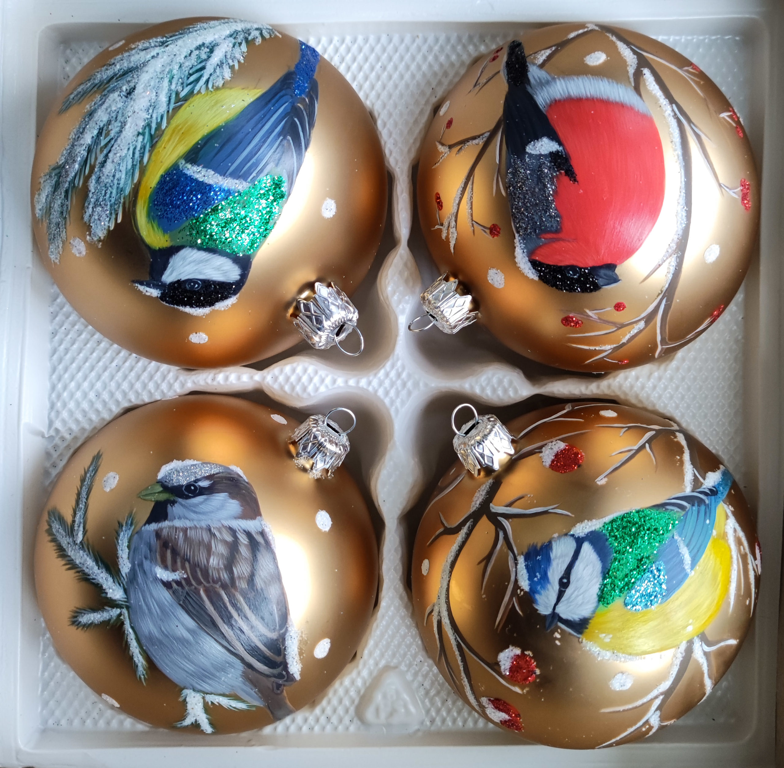 Cztery ręcznie malowane bombki z ptakami na gałązkach w kolorze złotym. Górna strona, od lewej: bogatka, gil. Dolna strona, od lewej: wróbel, modraszka.