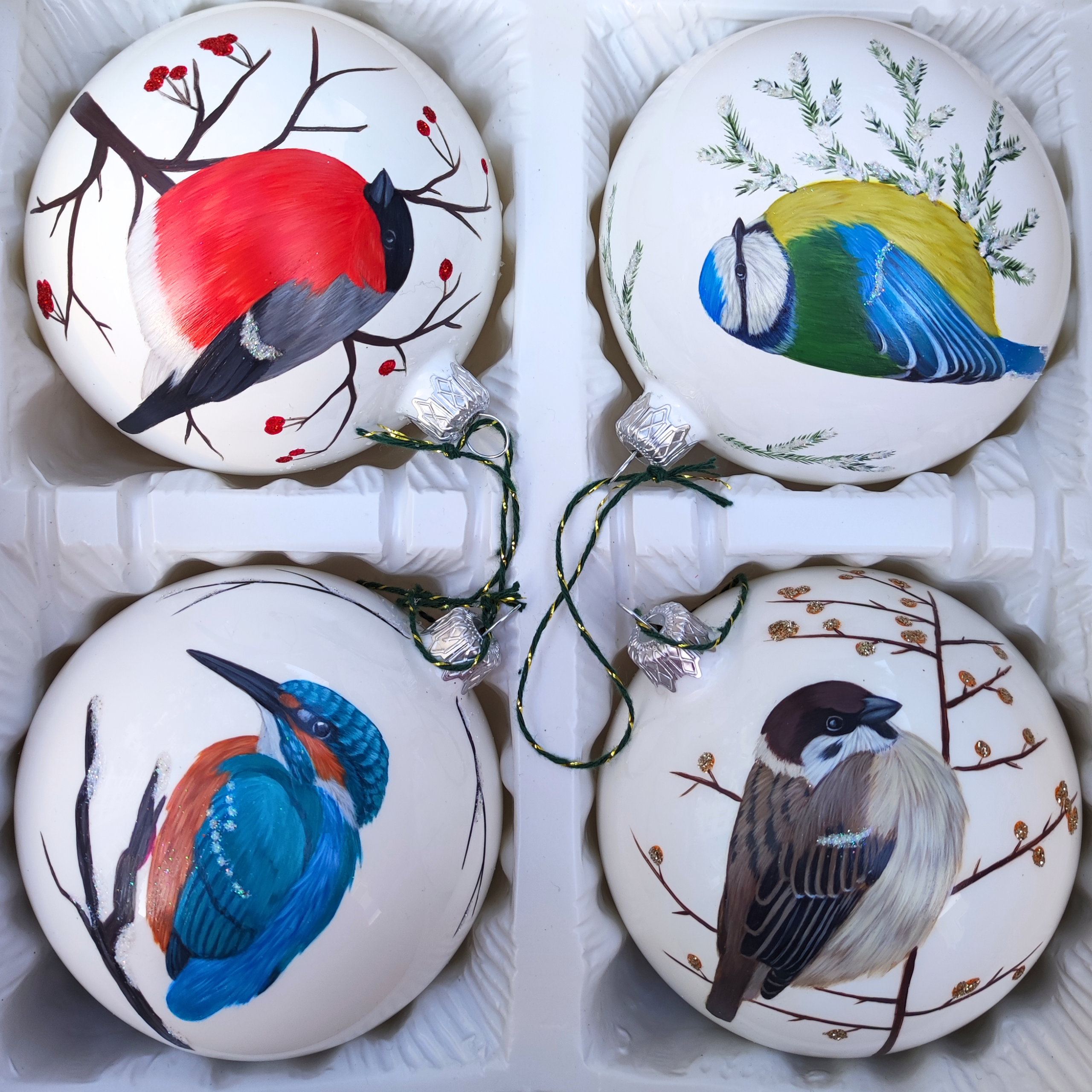 Komplet czterech białych bombek z ręcznie malowanymi ptakami: gilem, modraszką, zimorodkiem i mazurkiem.